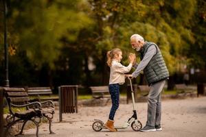homme âgé enseignant à sa petite-fille comment faire du scooter dans le parc photo