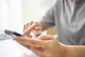 gros plan d'une femme tenant un téléphone portable dans ses mains et la messagerie texte alors qu'il était assis au bureau devant un ordinateur portable. photo