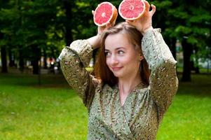 fille heureuse caucasienne avec pamplemousse s'amusant dans le parc. portrait d'été. vitamines photo