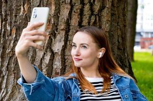 fille souriante aux cheveux rouges prenant selfie tout en écoutant de la musique.loisirs dans le parc.utilisation des technologies photo
