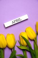 carte de pâques verticale avec tulipes et avril écrit sur un bloc de bois photo