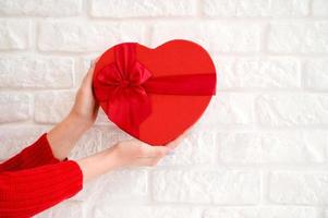 mains féminines donnant une boîte cadeau coeur rouge. photo