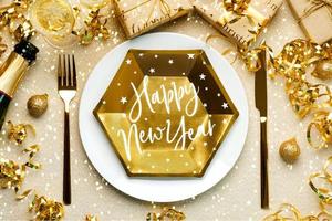 bonne année. vue de dessus de l'assiette pour le dîner de noël avec le texte bonne année, ornement de noël, couverts et bouteille de champagne. fond de concept de célébration du nouvel an photo