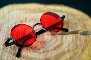 lunettes de soleil rondes avec lentille rouge sur un support en bois. photo