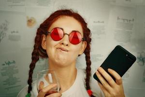 drôle de fille avec des nattes et des lunettes de soleil rouges fait des grimaces. photo