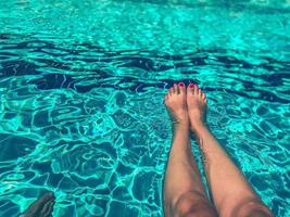 pieds d'une fille avec une pédicure lumineuse dans la piscine. nager dans l'eau d'un pays chaud et tropical. jambes minces dans la piscine photo