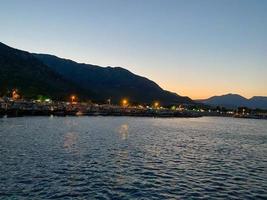 belle côte et plage avec des contours de montagnes sur fond de coucher de soleil depuis la mer ou l'océan et les lumières brûlantes de la ville photo