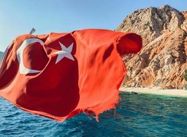 rocher au centre de la mer. une eau bleue avec de l'écume bouillonnante avec une grande et haute montagne au centre. le drapeau turc flotte au vent photo