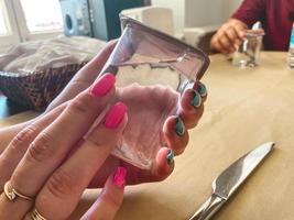 fille avec des bagues en or sur ses doigts et une manucure lumineuse. ongles bleus et roses. dans les mains d'une fille un verre transparent avec de l'eau propre et potable photo