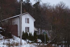 maison blanche debout sur une colline entre des arbres visibles de la route dans la neige de l'hiver photo