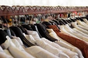 portants à vêtements en bois avec cintres et chemises blanches et brunes à l'intérieur d'un magasin. photo