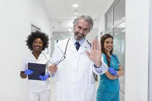 un groupe multiethnique de trois médecins et infirmières debout dans un couloir d'hôpital, portant des blouses et des blouses. l'équipe de travailleurs de la santé regarde la caméra et sourit photo