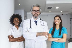 portrait d'un médecin caucasien souriant portant un uniforme médical blanc, un stéthoscope et des lunettes regardant la caméra posant dans une clinique privée, un homme heureux gp ou montrant de la confiance sur le lieu de travail à l'hôpital photo