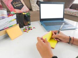 image de maquette, ordinateur portable avec écran vierge avec une femme prenant des notes sur du papier jaune avec un stylo dans la chambre de la maison moderne. maquettes d'ordinateur portable photo