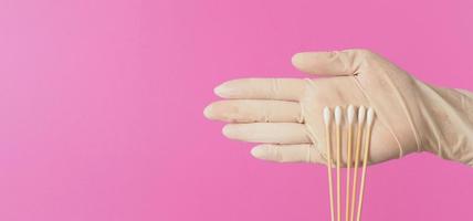 bâtonnets de coton pour test d'écouvillonnage dans la paume de la main avec des gants médicaux blancs ou un gant en latex sur fond rose. photo