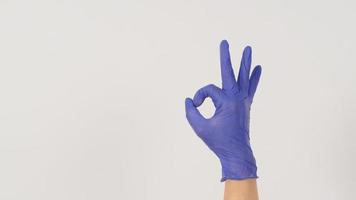 le signe de la main a-ok et portez un gant en latex violet ou violet sur fond blanc. photo