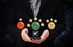 la main de la personne utilisant un smartphone donne une icône de sourire heureux et un symbole cinq étoiles pour augmenter la note du concept de produit et de service, l'expérience du service client et l'enquête de satisfaction commerciale. photo