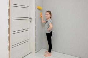 petite fille conduit le long du mur avec un rouleau à peinture dans une maison en cours de rénovation photo