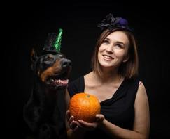 portrait d'un chien doberman avec une fille propriétaire. en costumes de carnaval avec une citrouille. photo