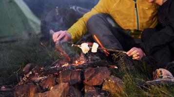 vue rapprochée des mains des gens qui tiennent des bâtons avec de la guimauve à l'extérieur près d'un feu de camp photo