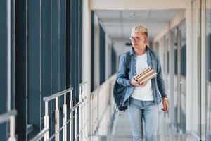 un jeune étudiant en jeans est dans le couloir d'un collège avec des livres dans les mains photo