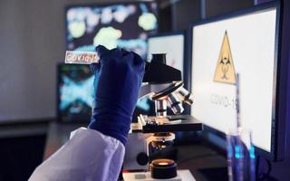 un scientifique en uniforme et des gants tiennent une lentille avec le titre covid-19 dessus. à l'intérieur en laboratoire photo