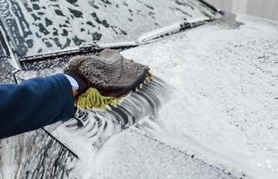 travailleur masculin en uniforme lavant une nouvelle voiture moderne pleine de savon. conception de services photo