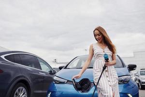 partie avant. femme sur la station de charge des voitures électriques pendant la journée. véhicule neuf photo