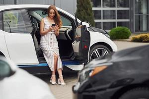 femme avec téléphone debout près de sa voiture blanche dans la rue photo