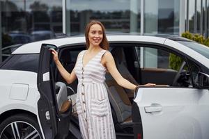 femme aux cheveux blonds se tient près de sa voiture blanche dans la rue photo