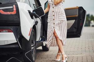 photo recadrée. femme sur la station de charge des voitures électriques pendant la journée. véhicule neuf