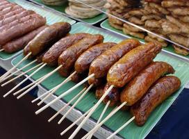 collation thaïlandaise, saucisses de porc et de riz de style thaïlandais du nord-est de la tradition, saucisses esan, grillées avec des bâtonnets de bois de brochette servis sur une feuille de bananier à vendre sur le marché thaïlandais de l'alimentation de rue photo