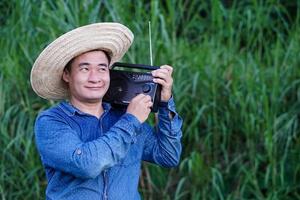 un fermier asiatique porte un chapeau, une chemise bleue, tient une radio transistor sur son épaule au jardin, se sent heureux. concept, heureux de travailler avec de la musique, des nouvelles, des informations de la radio. mode de vie campagnard. photo