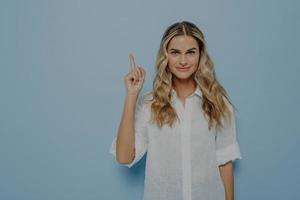 fille blonde calme avec un léger sourire pointant vers le haut dans l'air avec son doigt photo