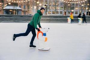 portrait d'un homme barbu heureux porte des vêtements à la mode utilise l'aide au skate pour garder l'équilibre sur la glace, profite des week-ends en cercle d'amis proches, pose devant la caméra. personnes, loisirs, concept de style de vie photo