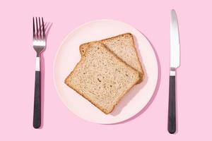 mise à plat de pain sandwich de blé entier sur assiette, fourchette et couteau sur fond rose photo