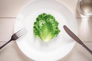 feuille de laitue verte sur une assiette, une fourchette, un couteau, un verre d'eau - concept de régime strict photo