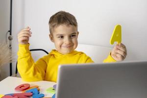 adorable, mignon, petit garçon apprenant l'alphabet en ligne, avec un ordinateur portable à la maison. enfant utilisant une plate-forme d'apprentissage en ligne pour passer un appel vidéo avec son professeur et étudier. enseignement à domicile et à distance pour les enfants photo