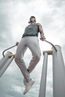 sportif travaillant sur l'équipement public sportif dans la salle de sport en plein air. un homme actif sportif dans un parc par temps nuageux. photo