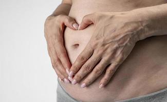 femme enceinte tient les mains sur le ventre sur un fond bleu. concept de grossesse, de maternité, de préparation et d'attente. gros plan, à l'intérieur. belle