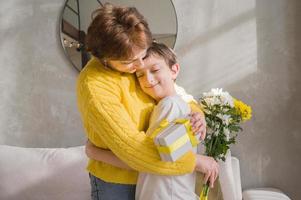 mère étreignant son fils enfant comme tenant un cadeau et un bouquet de fleurs.la fête des mères ou des femmes photo