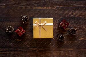 vacances d'hiver à plat avec une petite boîte cadeau dorée entourée de petits cadeaux et de cônes aux couleurs sombres. vintage noël ou nouvel an photo