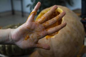 femme sculptant une grande citrouille orange pour halloween alors qu'elle était assise à une table en bois à la maison photo