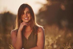 portrait d'une fille heureuse qui se tient dans le champ éclairé par la lumière du soleil photo