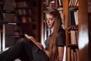 est assis sur le sol. une étudiante est dans une bibliothèque pleine de livres. conception de l'éducation photo