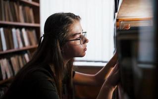 la recherche de la bonne information. contre fenêtre. une étudiante est dans une bibliothèque pleine de livres. conception de l'éducation photo