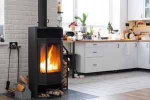 l'intérieur festif de la maison est décoré pour noël et le nouvel an dans un style loft avec poêle noir, cheminée, arbre de noël. studio chaleureux avec cuisine blanche, bois brûlant, cosy et chauffage de la maison photo