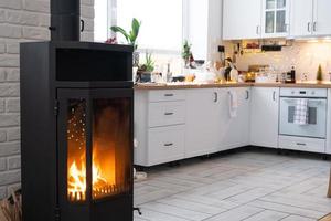 l'intérieur festif de la maison est décoré pour noël et le nouvel an dans un style loft avec poêle noir, cheminée, arbre de noël. studio chaleureux avec cuisine blanche, bois brûlant, cosy et chauffage de la maison photo