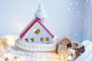 la maison confortable est enveloppée dans un chapeau et une écharpe dans un décor de rebord de fenêtre de tempête de neige. hiver, neige - isolation de la maison, protection contre le froid et les intempéries, système de chauffage des locaux. ambiance festive, noël, nouvel an photo