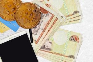 Billets de 100 pesos dominicains et bitcoins dorés avec smartphone et cartes de crédit. concept d'investissement en crypto-monnaie. minage ou commerce de crypto photo